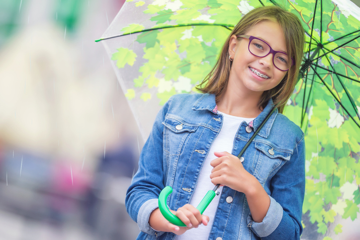 smiling girl with umbrella, glasses, and braces from Robinson Orthodontics in Grants Pass, OR